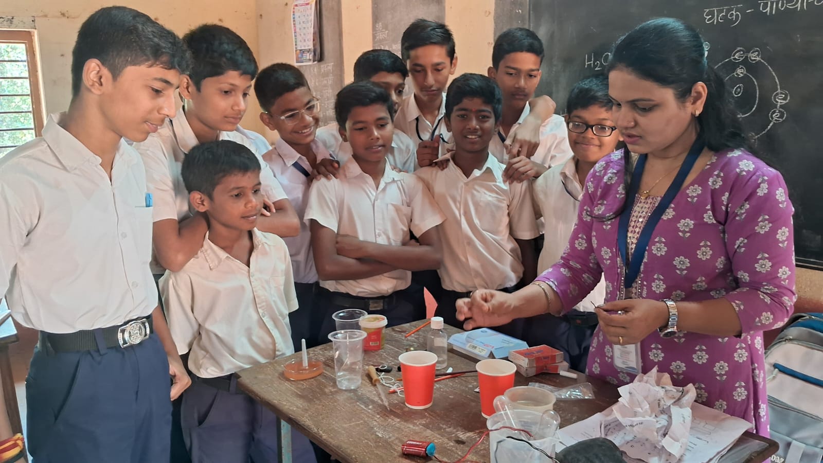 A teacher performing an experiment with a group of children surrounding her.