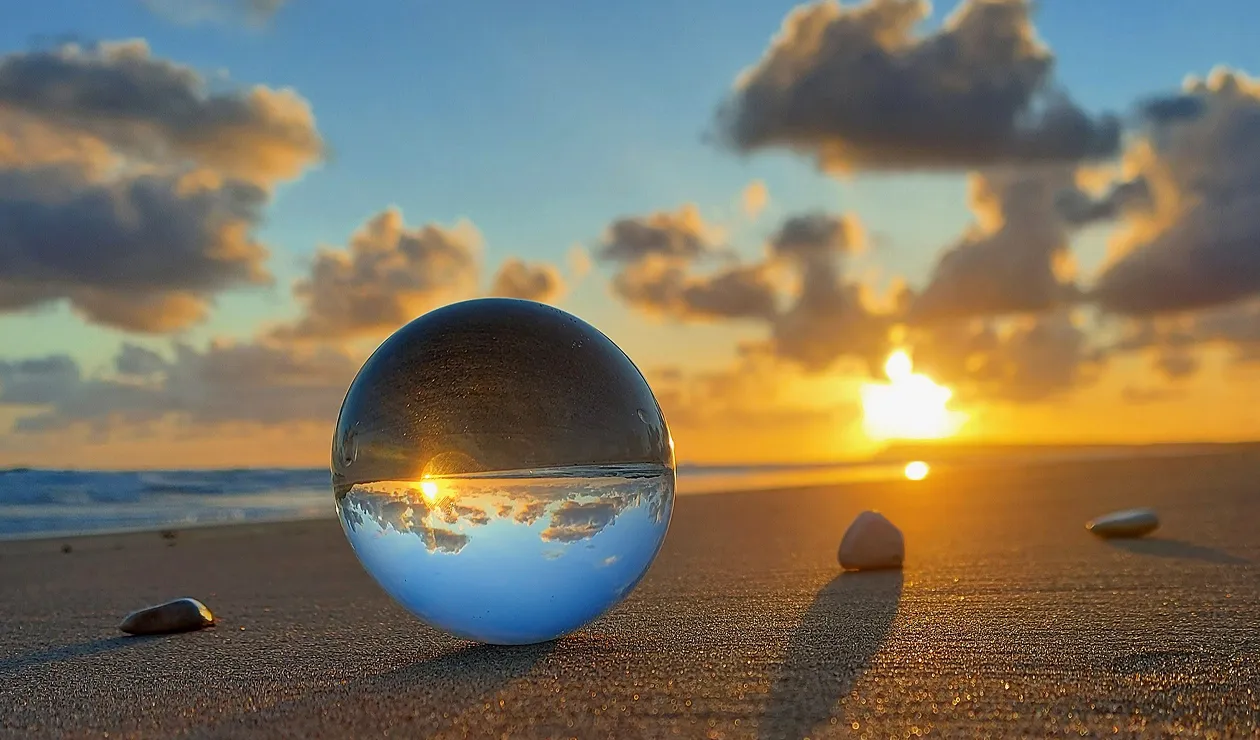 Details image depicting a drop of water which is against a beach. The drop shows a reverse image of the beach.